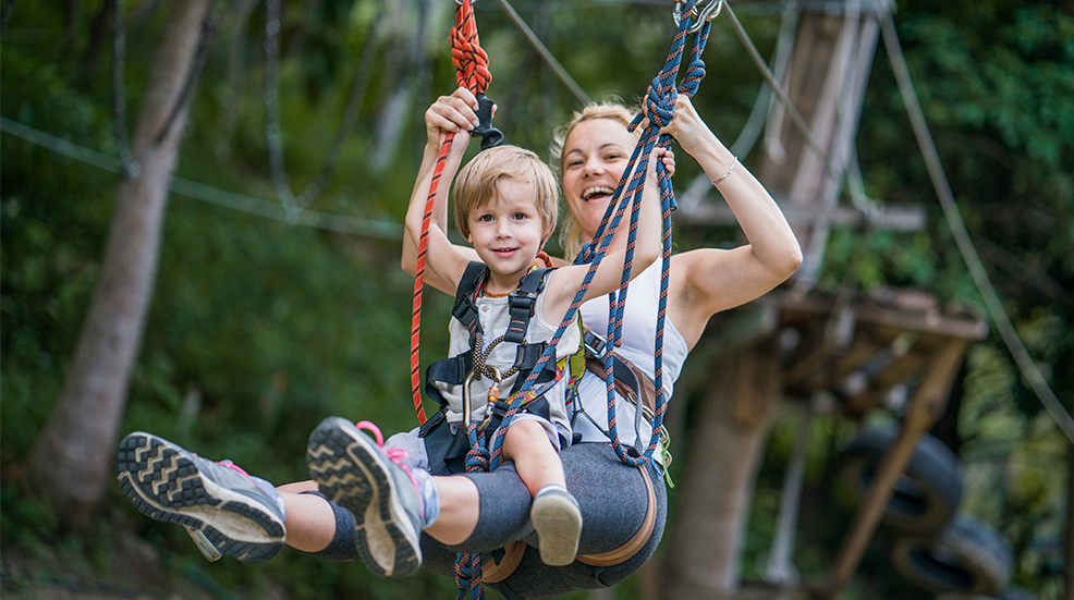 Happy mother and son having fun while zip lining in the forest